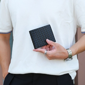 Close-up of men's black woven leather bifold wallet held by hand showing fine texture