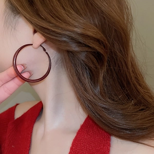 Detailed close-up of a large deep red glazed hoop earring worn on a model with curly hair