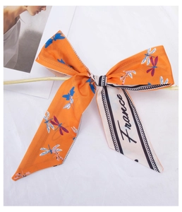 Detailed view of an orange silk hair scarf featuring a dragonfly pattern and a bow tie