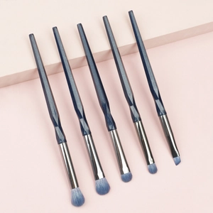 Close-up of 5 blue glitter eye makeup brushes with faceted handles on pink platform