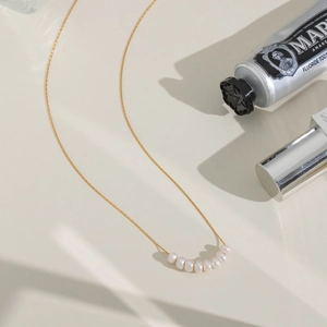 Detailed view of a gold chain necklace with curved natural white pearls on a beige surface