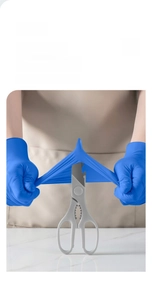 Blue nitrile gloves demonstrated with scissors to show puncture resistance and high elasticity