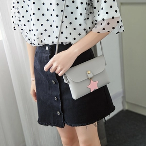 Light gray small crossbody bag with pink star charm worn by a fashion model