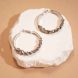 Close-up of silver geometric hoop earrings with sequin texture on white plaster tray