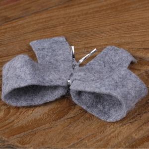 Detail view of a gray felt bow ornament with silver metal wire on a dark wood surface