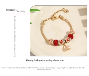 Close-up of a gold snake chain bracelet with red crystal beads and lotus flower pendant