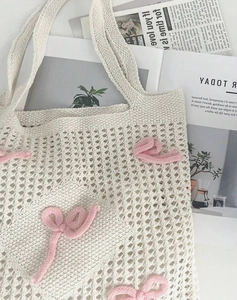 Close-up of cream knit bag with pink 3D bow detail and hollow weave texture