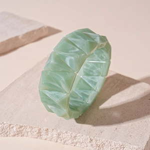 Detail of green marble acrylic resin geometric bangle on light sandstone rock prop