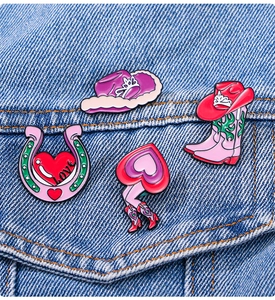 Détail de pin's en émail rose (chapeau, botte et fer à cheval) sur tissu denim
