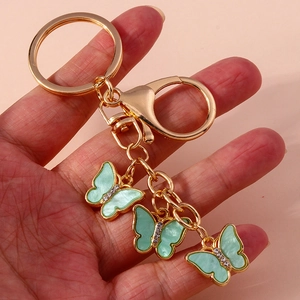 Macro detail of three light green butterfly charms on a golden metal keychain with crystals