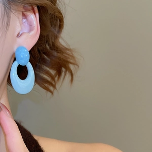 Detail of light blue acrylic oval earrings worn by a model in a minimalist style