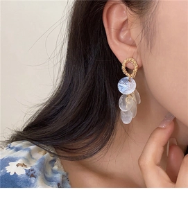 Close-up of golden round shell tassel earrings worn by model for a bohemian look