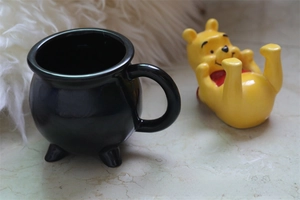 Close-up of a black ceramic cauldron-shaped mug with three legs and a smooth glossy glaze