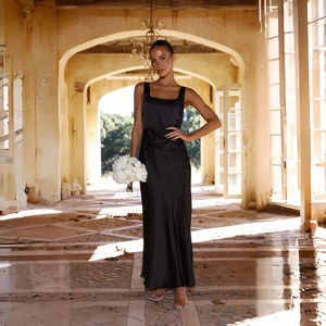 Elegantes schwarzes Satin-Maxikleid mit eckigem Ausschnitt und breiten Trägern vor Rundbogen