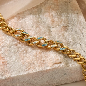 Gold plated evil eye Cuban chain bracelet with blue enamel detail on a stone surface
