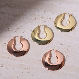 Polished chunky hollow C-shaped hoop earrings in gold and rose gold on stone surface