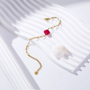Detail of gold paperclip chain bracelet with a faceted magenta stone and lobster clasp