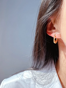Close-up of golden U-shaped hoop earrings with relief patterns on model's ear