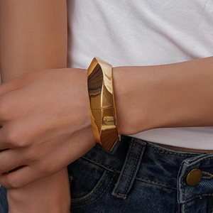 Close-up of a wide chunky gold geometric metal cuff bracelet worn by a model