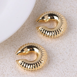 Macro detail of gold-plated twisted C-shape ear cuffs with textured ridges on stone surface