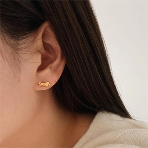 Close-up of minimalist golden bow earrings worn by a model for a stylish look