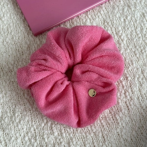 Pink towel fabric headband with golden metal charm on soft white knit background