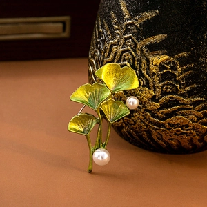 Detail of elegant gold-green ginkgo leaf brooch with white pearls on a dark base
