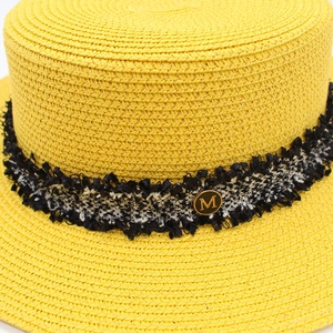 Detailed macro view of yellow woven straw boater hat with tweed band and M metal badge
