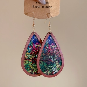Detailed macro of teardrop wood earrings featuring colorful mosaic art on display card