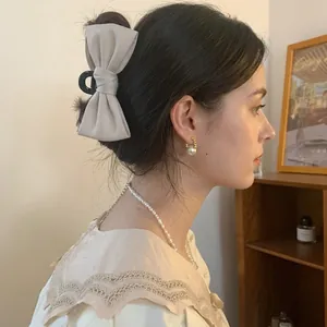 Elegant beige bow hair claw clip for women worn by a model in a warm home setting