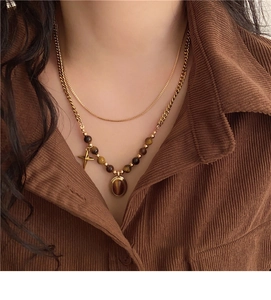 Close-up of layered necklace with brown tiger eye stone and cross pendant on gold chains