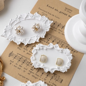 French retro display of pearl flower and rectangle earrings on a white plaster relief tray