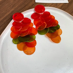Detail view of colorful shell drop earrings with tiered gradient discs in a ceramic bowl