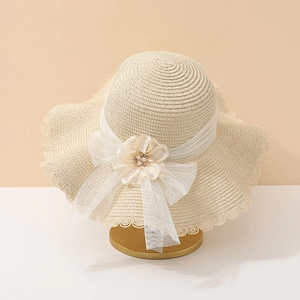 Détail d'un chapeau de paille beige à large bord avec fleur en dentelle et perles blanches