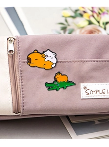 Detail of cute Capybara and crocodile enamel pins displayed on a purple canvas bag