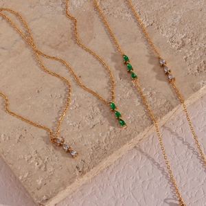 Detail of 18K gold teardrop pendant necklaces with emerald and white gemstones