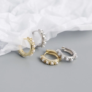 Close-up of gold and silver hoop earrings with small pearls on white paper
