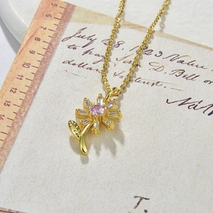 Macro detail of golden sunflower pendant with pink center and white zircon stones