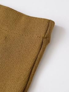 Détail du tissu en maille jaune moutarde montrant les coutures précises et la texture