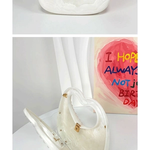 Detail of white pearlescent heart-shaped evening bag with pearl trim and gold clasp