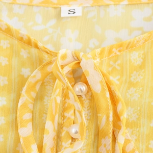 Yellow French floral chiffon dress with tie-neck design and pearl buttons in a close-up view