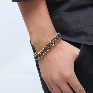 Détail d'un bracelet tressé en cuir noir et chaîne en acier inoxydable doré au poignet