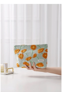 Close-up of light blue canvas makeup bag with orange poppy print and H&R logo
