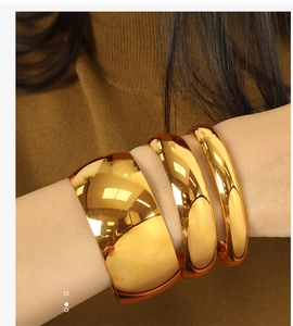 Macro detail of three polished gold titanium steel bangles stacked on a model wrist