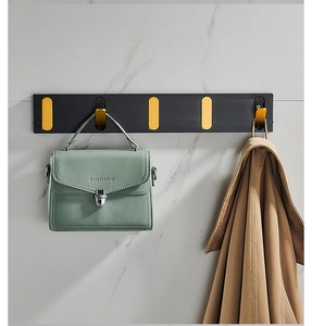 Foldable black and gold wall rack with five hooks holding a bag and a coat on a marble wall