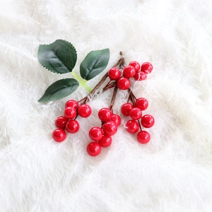 Close-up of artificial red berries branch with green leaves on white plush background