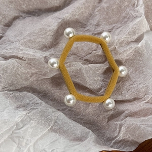 Close-up of ginger yellow elastic hair tie with white faux pearls on textured paper