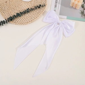 Close-up of a white silk bow hair clip with long ribbons in a minimalist lifestyle setting