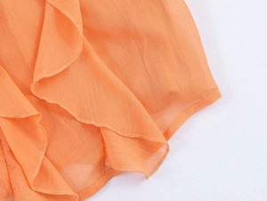 Detail of orange chiffon shirt featuring elegant ruffled edges and crepe fabric texture