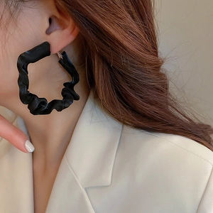 Close-up of a woman wearing large black geometric earrings with a unique wrinkled fabric texture